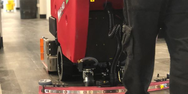 A floor cleaning machine in use by a worker indoors.