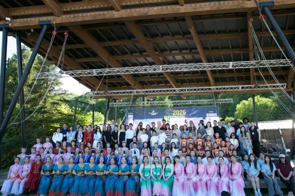 Large group photo under a wooden roof with colorful traditional dresses and casual wear.