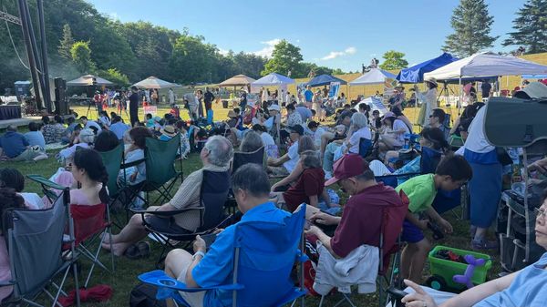 People enjoying an outdoor event with tents and chairs on a sunny day.