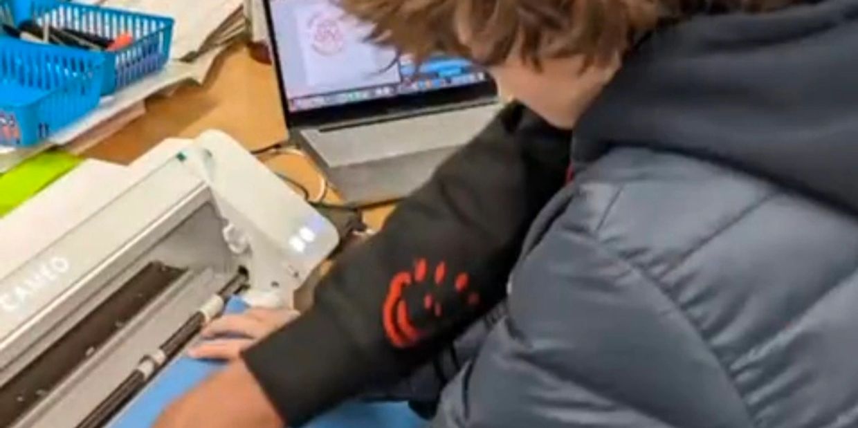 Person using a Cricut machine connected to a laptop for crafting.