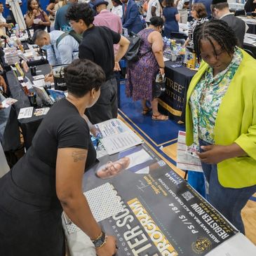 People exploring booths and materials at an indoor event or expo.