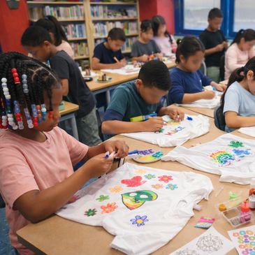 Children decorating white t-shirts with colorful designs in a classroom.