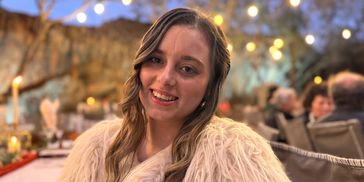 Smiling woman in a cozy fur coat at an outdoor evening event with string lights.