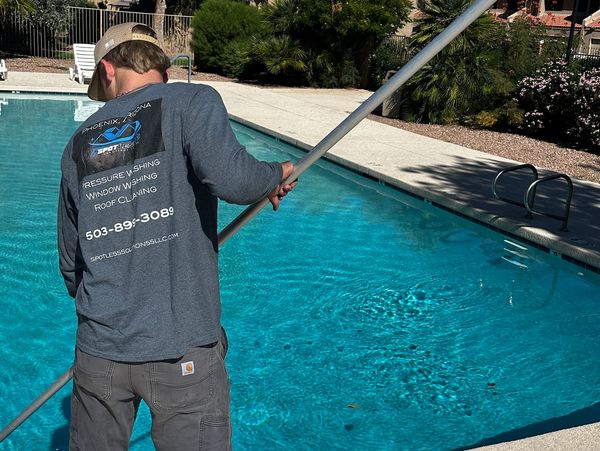 Man cleaning pool with long pole under clear blue sky.