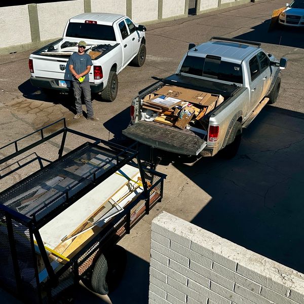 Two pickup trucks loaded with cardboard and a man standing beside one truck in a sunny parking lot.