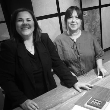 Two smiling women standing at a table indoors.