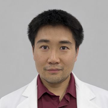 Man wearing a white coat and maroon shirt looking at the camera.