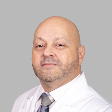 Portrait of a bald man in a white coat and tie against a gray background.