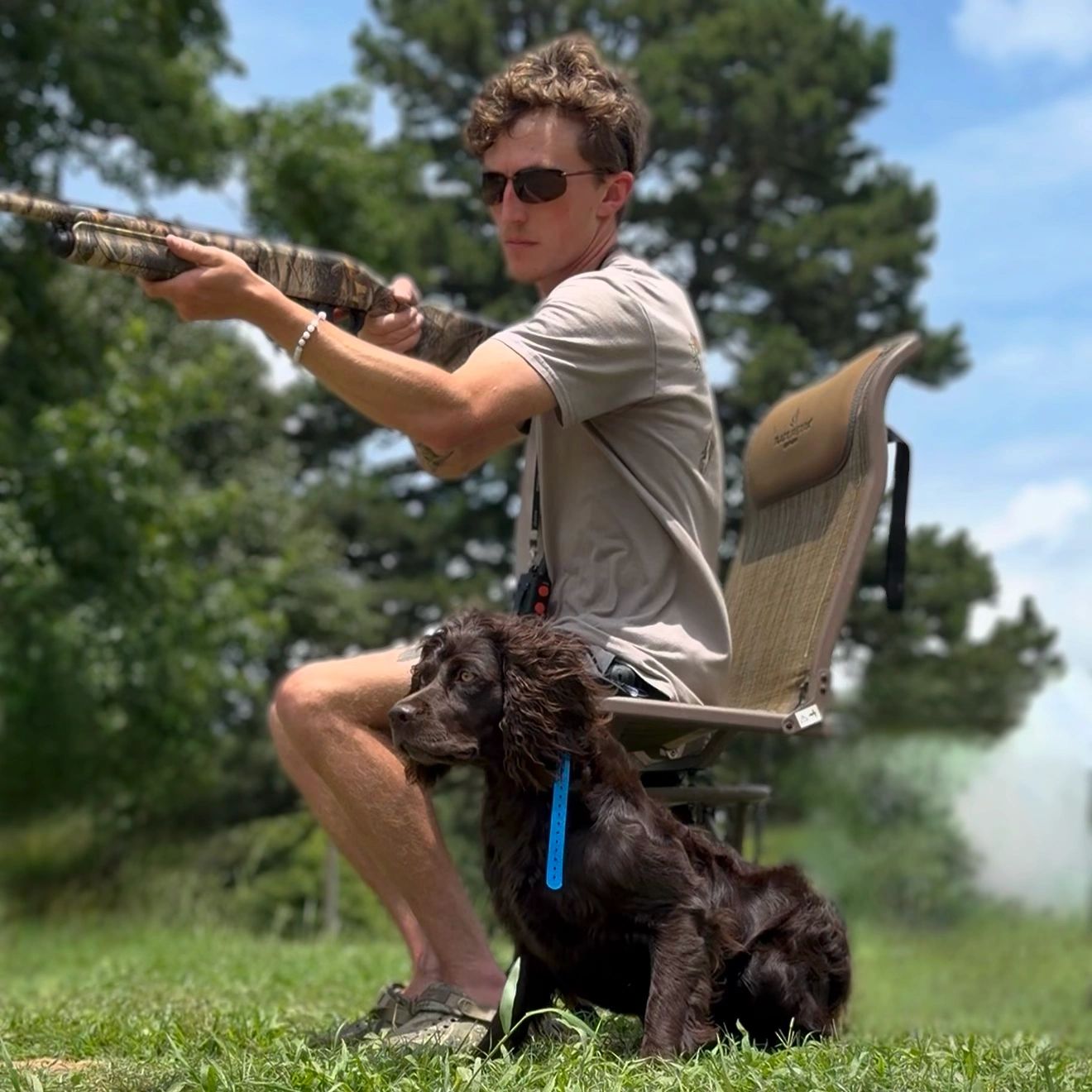 Man aiming a shotgun with a dog sitting nearby.