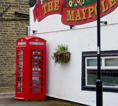 Classic red British telephone booth outside a building with a hanging flower basket.