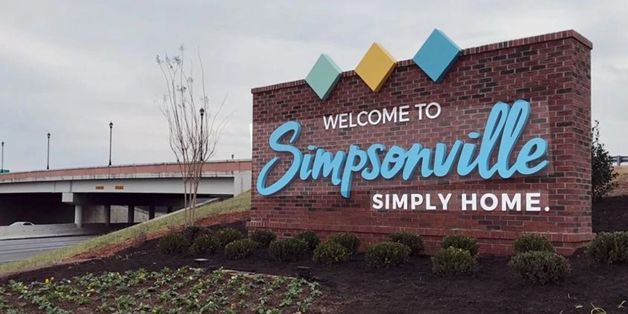 Brick sign welcoming visitors to Simpsonville with colorful diamond accents.