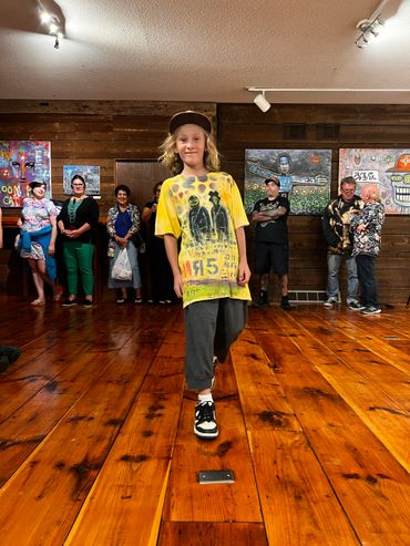 Young boy confidently walks on a wooden floor in an art gallery.