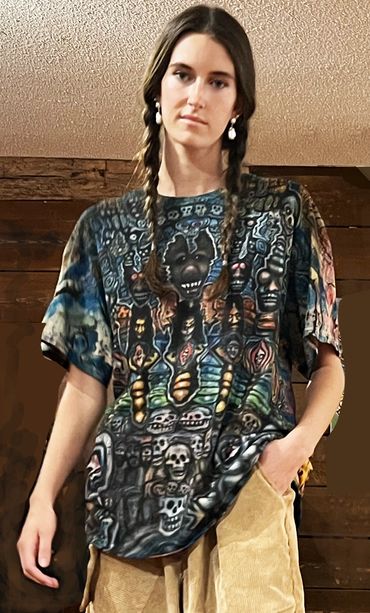 Young woman with braided hair wearing a colorful, skull-themed graphic shirt and beige pants.