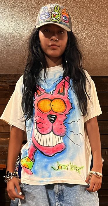 Person wearing a colorful cartoon cat t-shirt and a quirky illustrated cap.