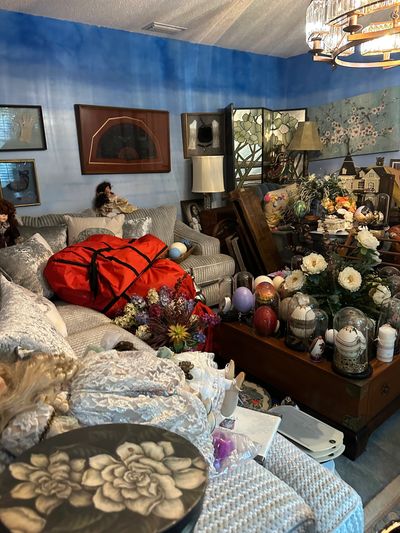 Cluttered living room with dolls and floral decorations.
