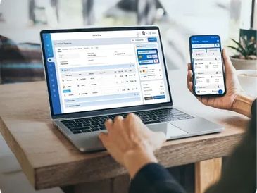 Person using a laptop and smartphone displaying a business or management software interface.