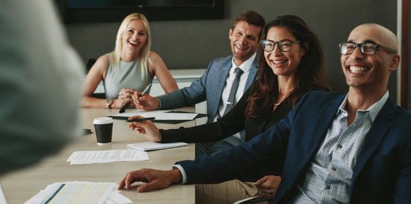 Four professionals smiling and engaged in a meeting around a conference table.