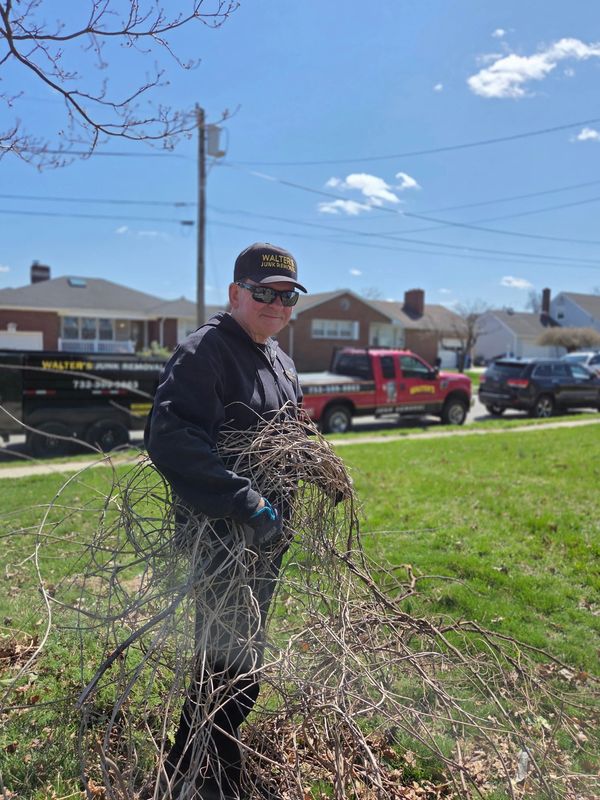 Man wearing Walter's Junk Removal uniform holding dry branches outdoors.