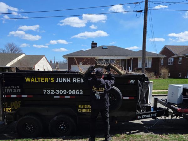 Person loading debris into Walter's Junk Removal trailer under a clear sky.