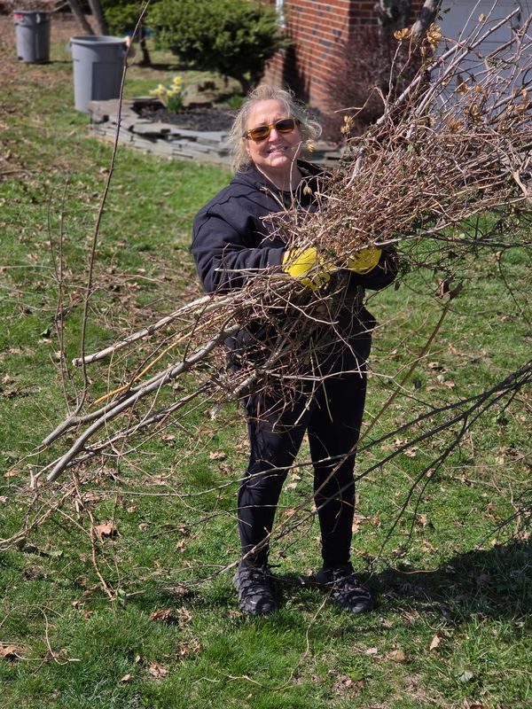 Woman in sunglasses holding a bundle of dry branches outdoors.