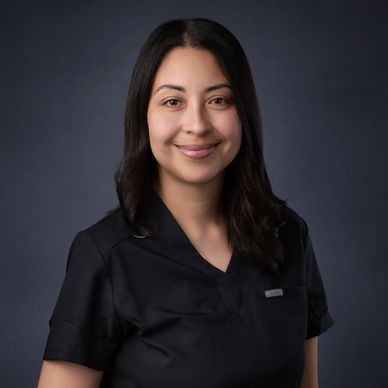 A woman in black scrubs smiling against a dark background.