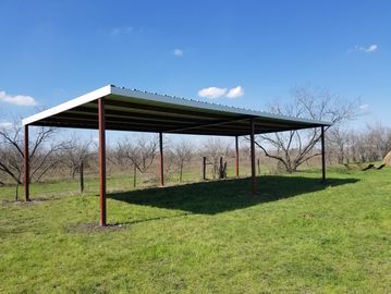 A metal carport structure on a grassy field under a blue sky.