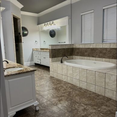 Spacious bathroom with tiled bathtub and dual sinks under bright lighting.