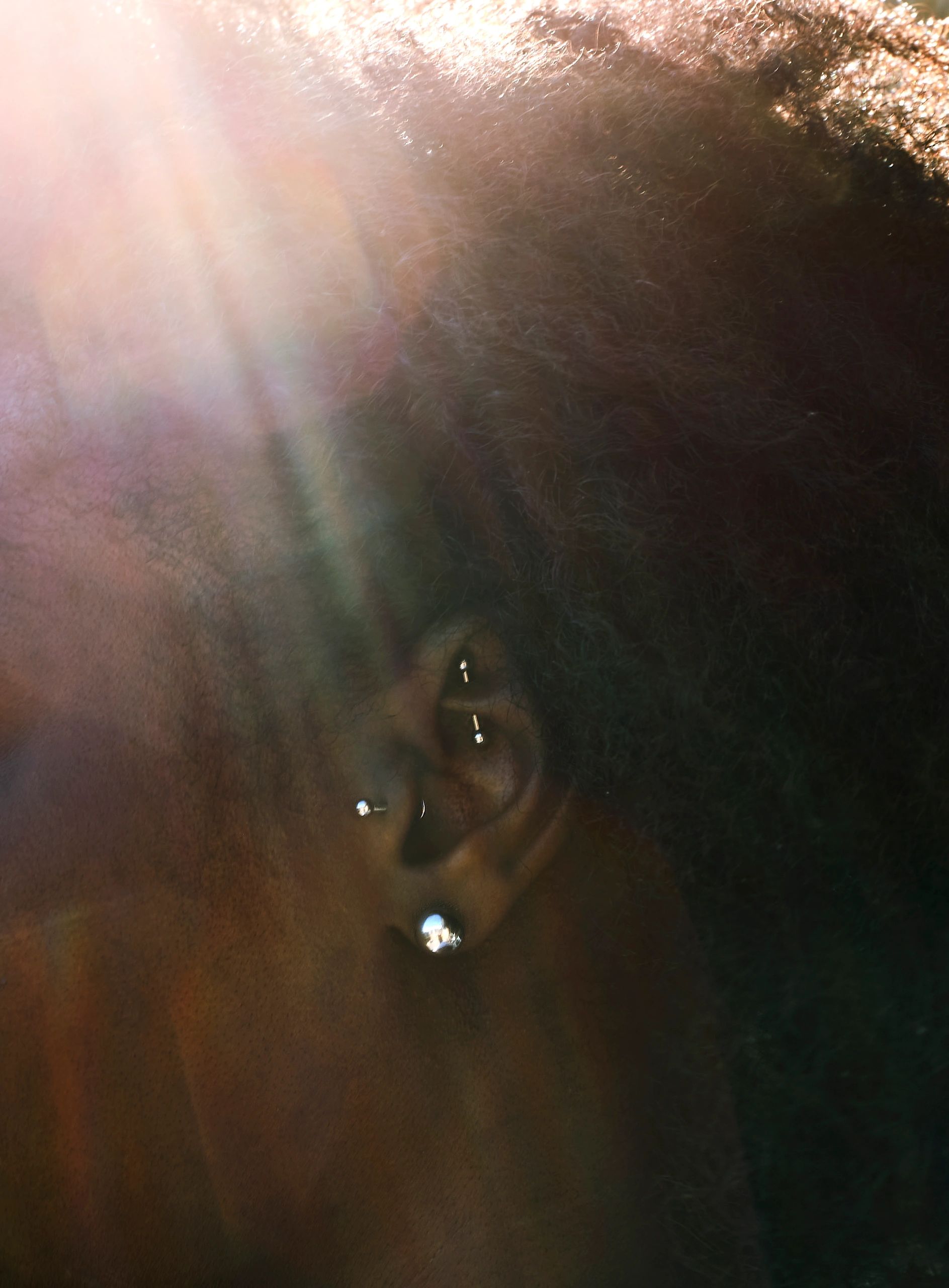 Close-up of ear with multiple silver earrings and natural hair.