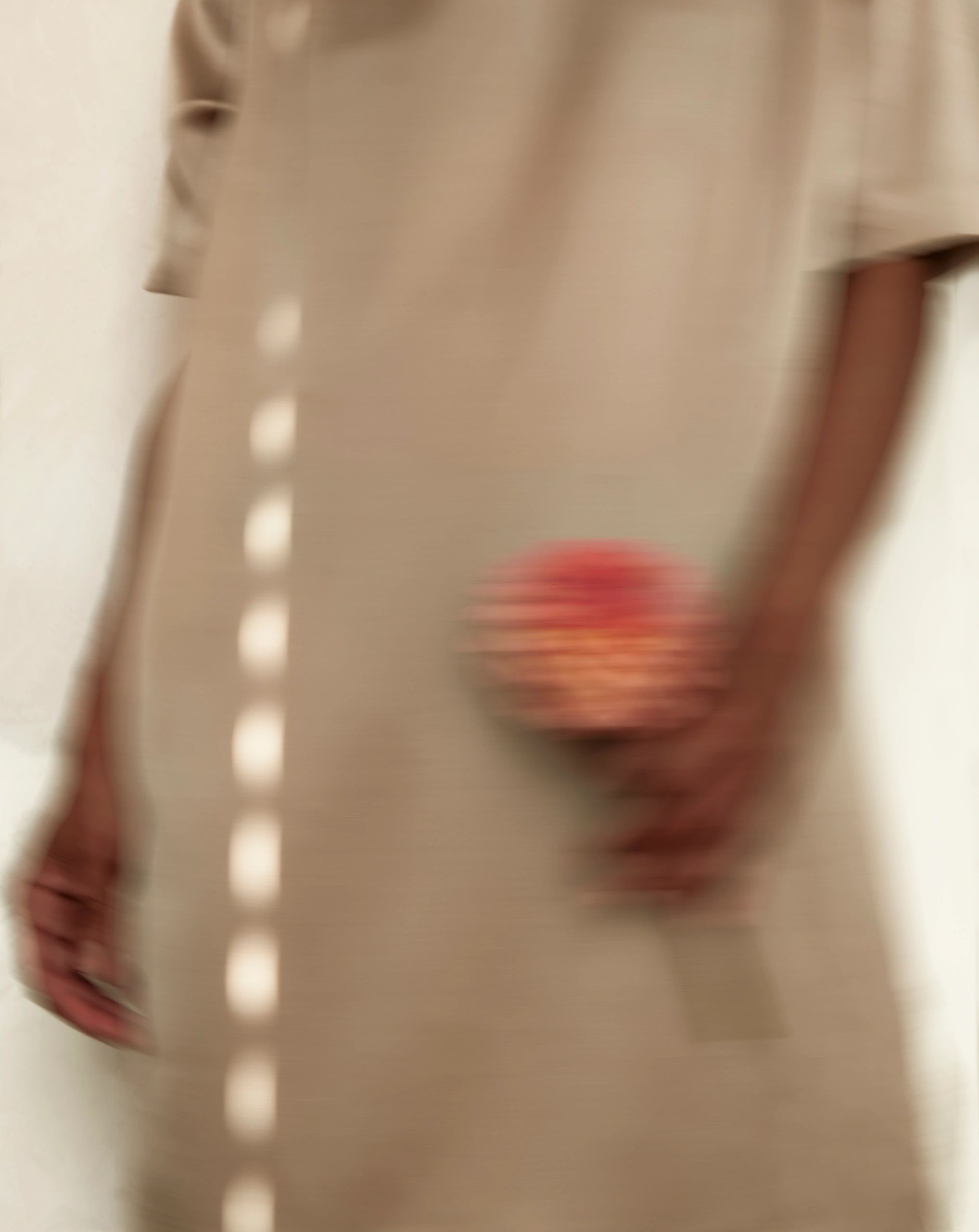 Blurred image of a person in beige clothing holding a red object.