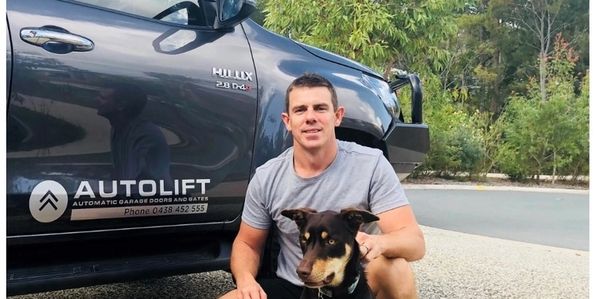 Man crouching with a dog beside a black Hilux truck with AUTOLIFT logo.