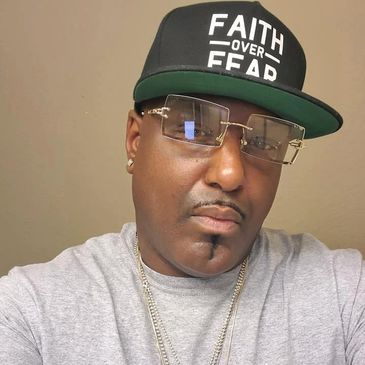Man wearing a black cap with 'Faith Over Fear' and gold-rimmed glasses.