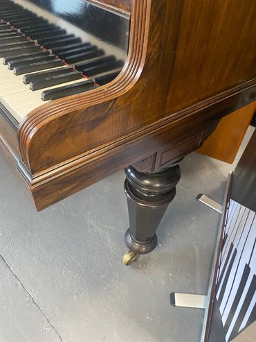 Close-up of an antique piano leg and keys.
