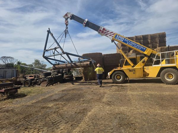Yellow crane lifting farm equipment with a worker guiding it on a sunny day.