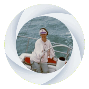 Smiling person steering a sailboat on the water.