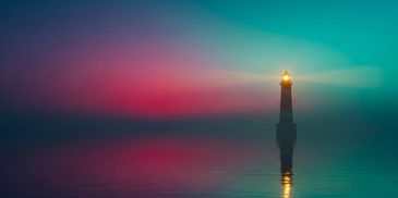 Lighthouse glowing in foggy twilight over calm water.