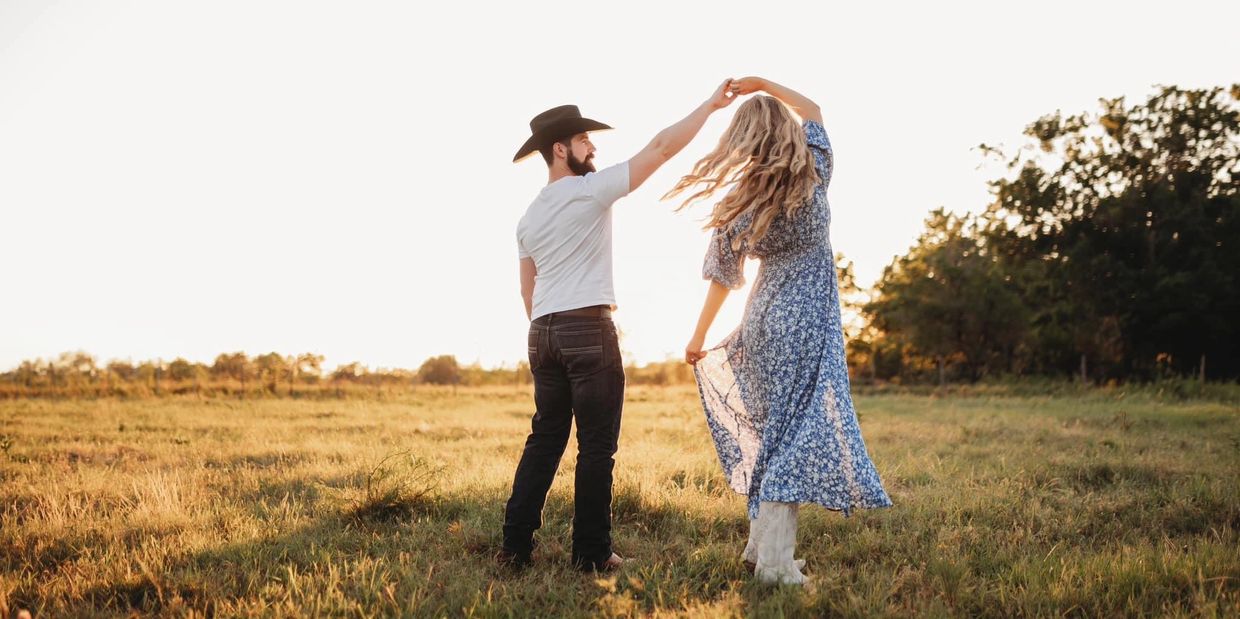 Couple dancing in a sunlit field at sunset, embracing a joyful moment.