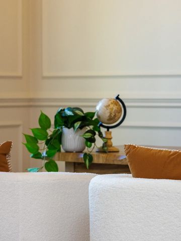 Cozy living room corner with white sofa, orange cushions, green plant, and a globe on a wooden table.