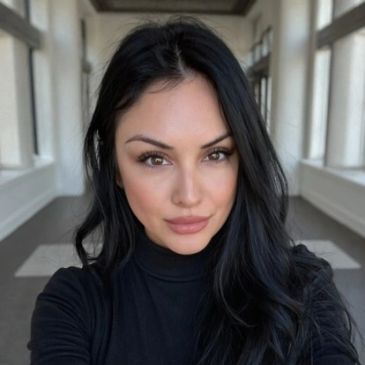 Woman with long black hair taking a selfie indoors.