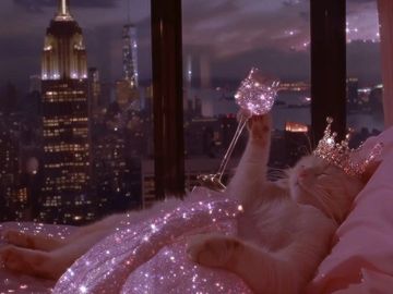 A cat with a crown lounges with a sparkling glass against a city nightscape.