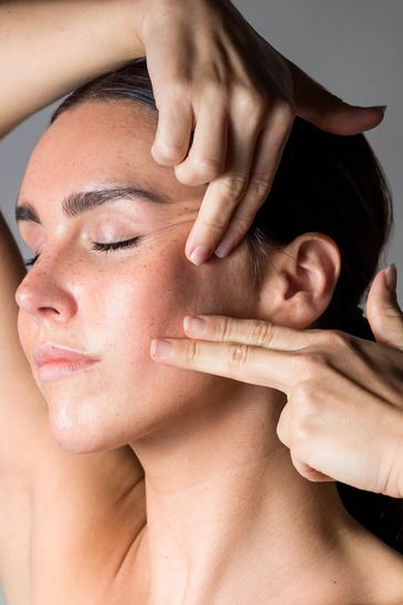 Woman performing facial massage with fingers on her cheek.