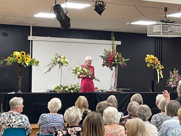 An elderly woman presents floral arrangements to an audience.