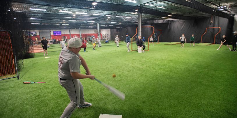 Young players practice baseball indoors on artificial turf.