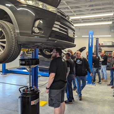 Group of men inspecting a car on a lift in a garage.