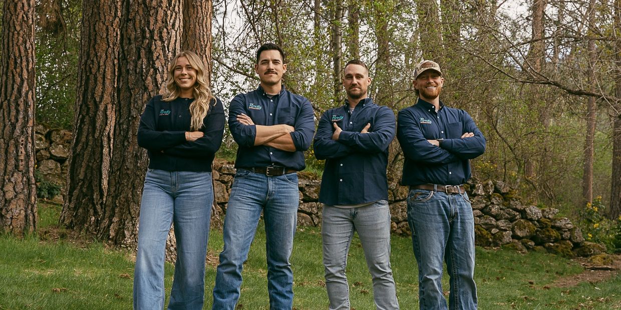 Four people standing outdoors with arms crossed, wearing matching shirts and jeans.