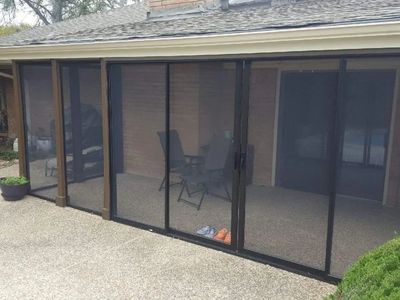 Screened patio with chairs and table behind mesh doors.