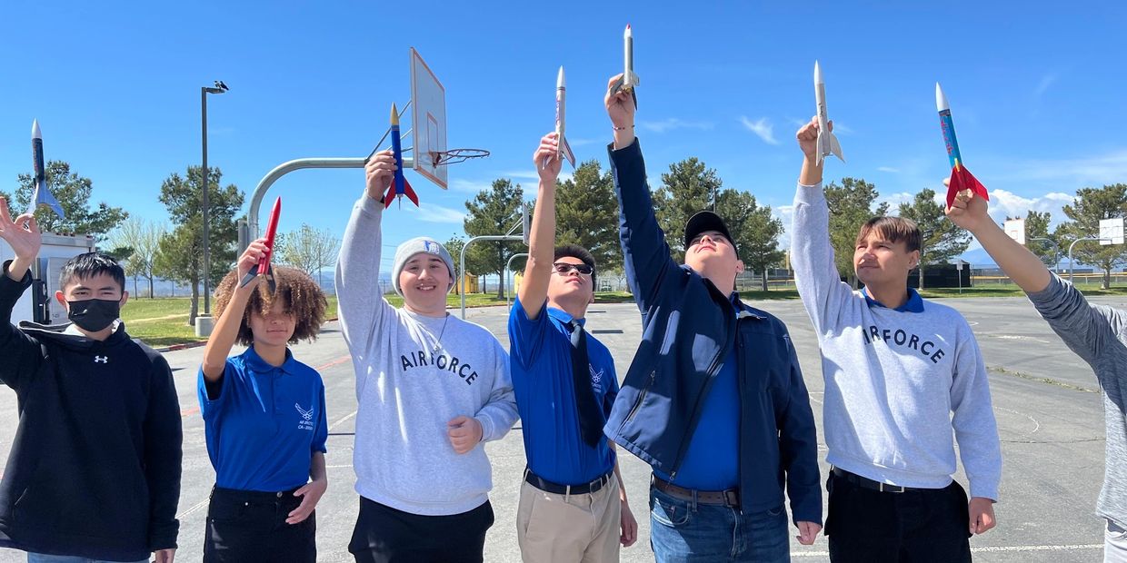 A group of young people holding model rockets outdoors on a sunny day.
