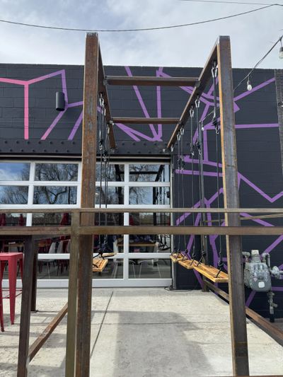 Outdoor wooden swings in front of a building with purple geometric wall art.