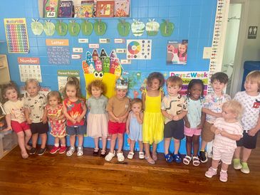 A group of children standing in a colorful classroom with educational posters.