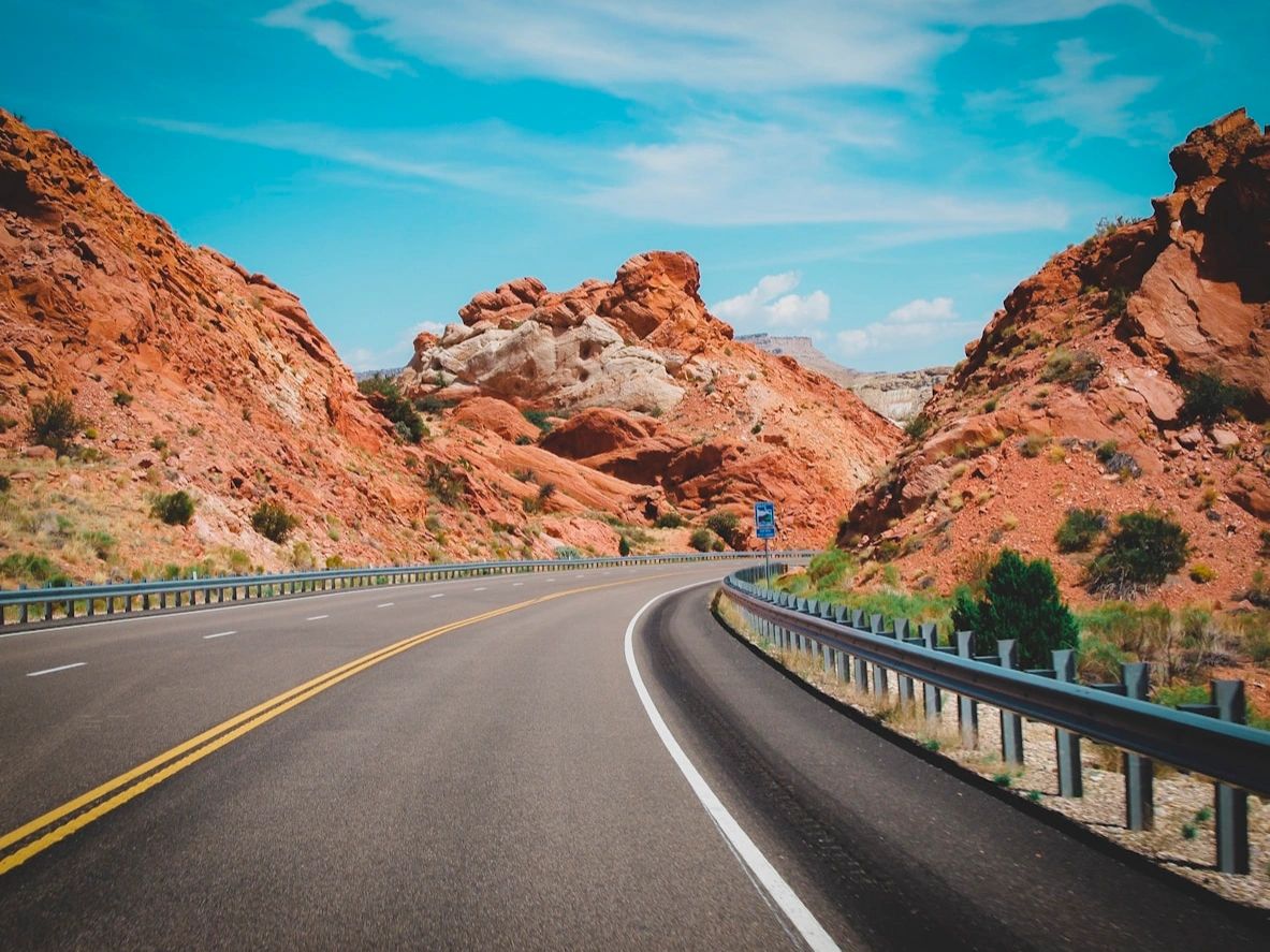 Curving highway through red rock desert under a bright blue sky.