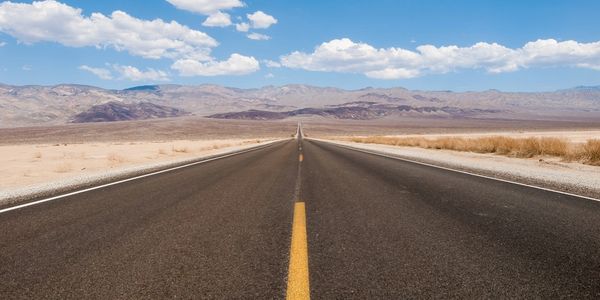A straight desert highway under a blue sky with scattered clouds.